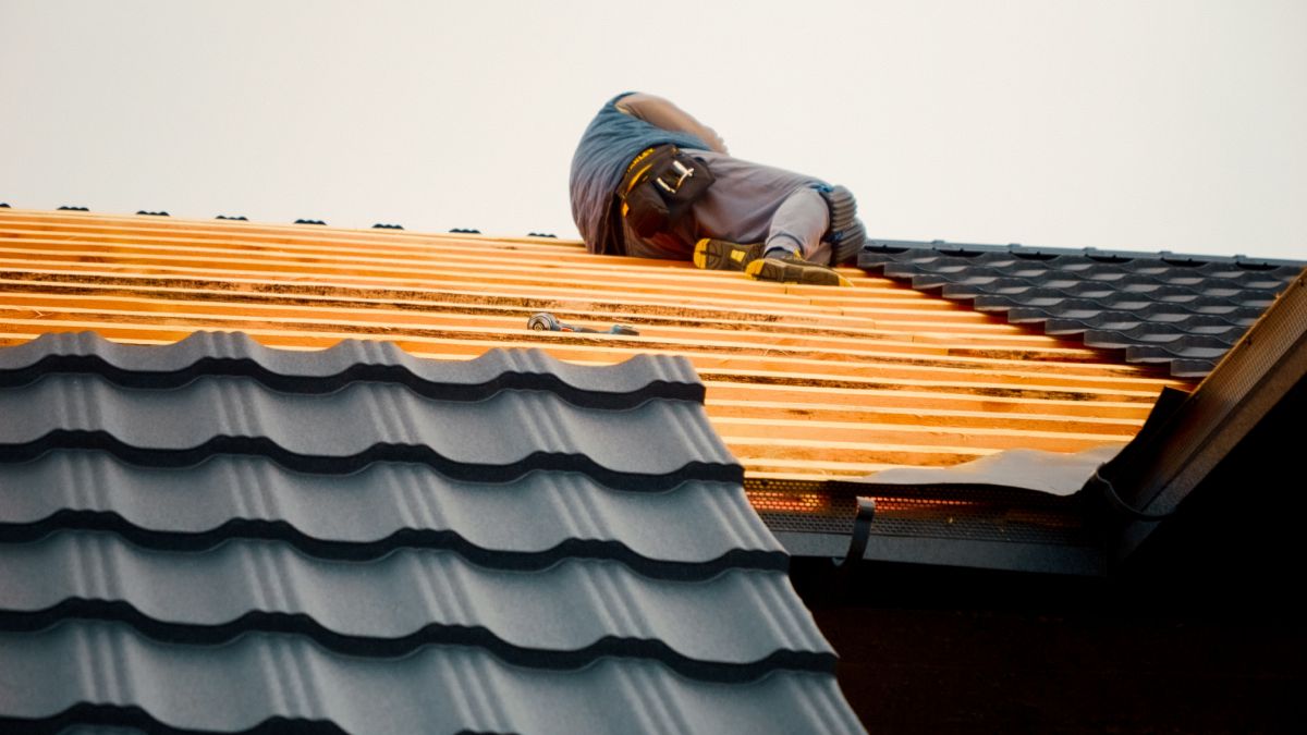 Les ouvriers ajoutent des tuiles métalliques et des feuilles anti-condensation au toit d'une maison en construction. Ce processus est essentiel pour la durabilité et l'isolation.