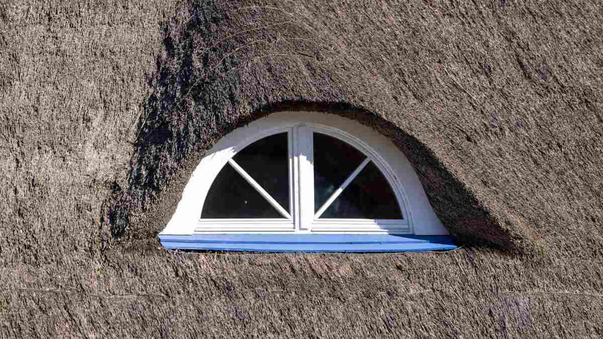 Toiture en chaume avec une petite fenêtre aux châssis blancs.