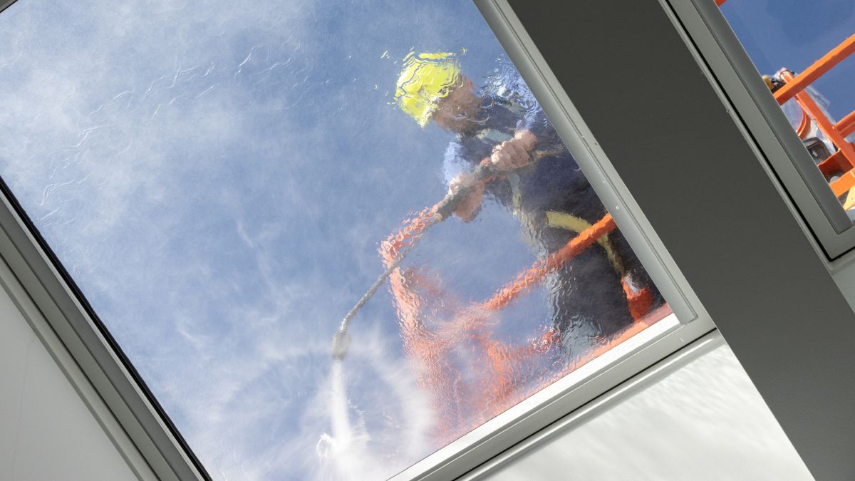 Travailleur sur un sélecteur de cerise nettoyant le toit d'une habitation avec un jet d'eau haute pression. 
