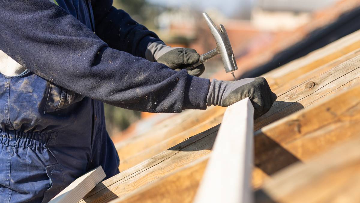Travailleur de charpentier de couvreur de construction clouant le panneau de bois avec marteau sur le travail d'installation de toit.