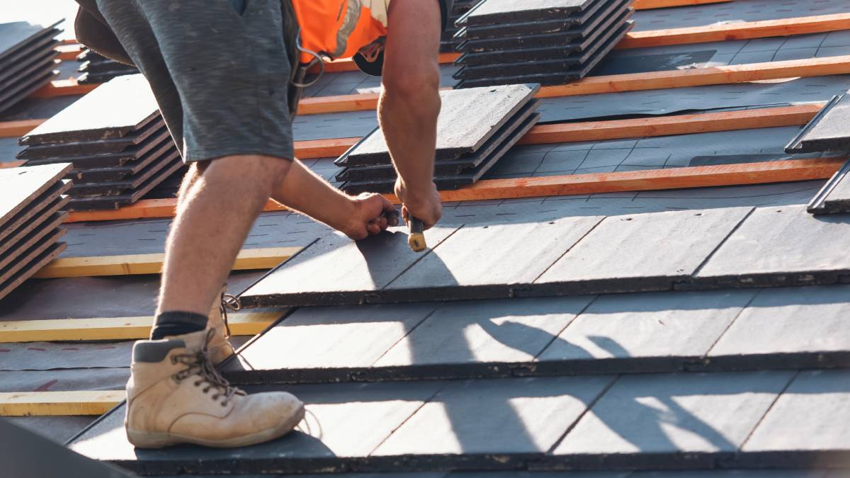 Un couvreur pose des tuiles sur un chantier à l'aide d'outils à main afin de garantir un alignement et une stabilité corrects sur une surface en pente.