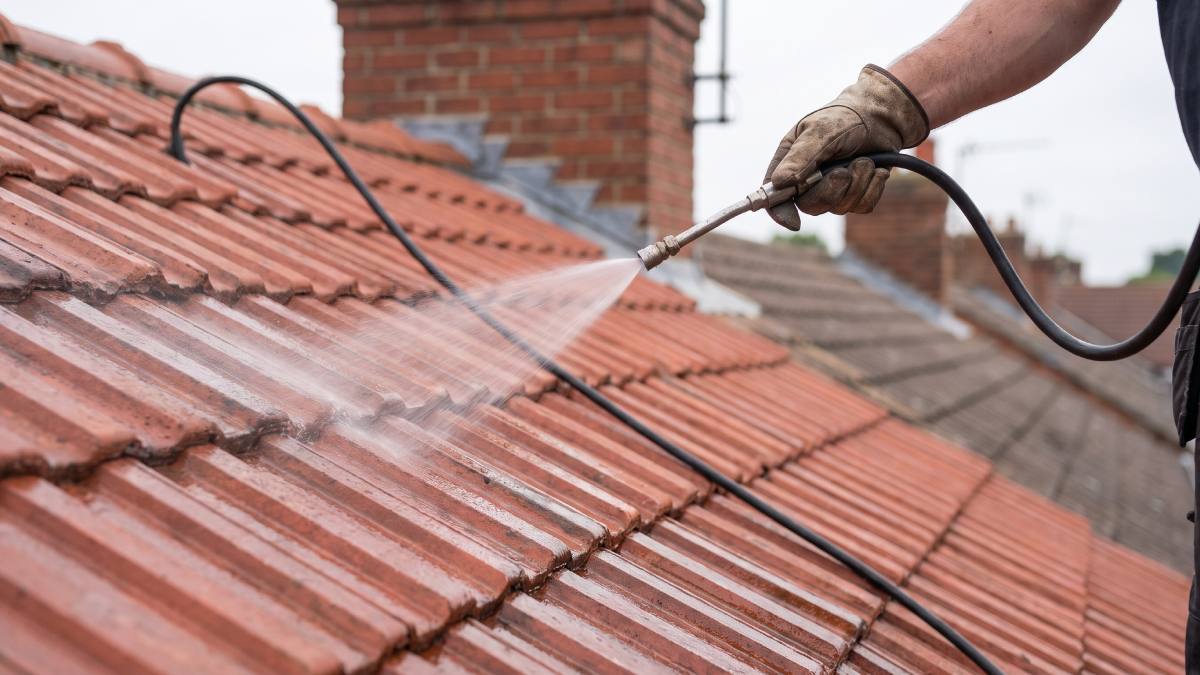 Vue de près d'un couvreur appliquant un produit hydrofuge sur des tuiles d'un toit d'une habitation en Belgique.
