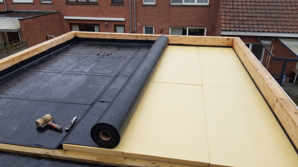 Pose d'une membrane sur une toiture plate durant une météo pluvieuse.