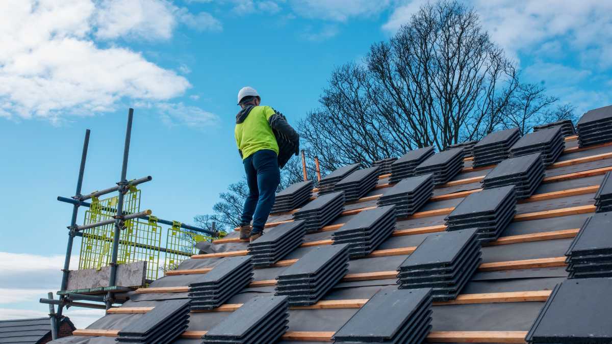 Un ouvrier en construction installe des tuiles sur le toit en ardoise sur la ,nouvelle maison sous un ciel ensoleillé.